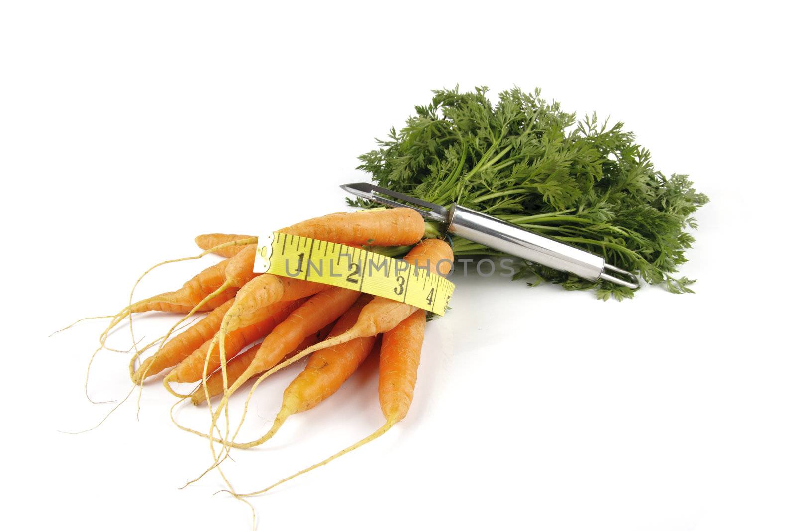 Fresh young bunch of carrots with green leafy stems and tape measure and chrome peeler on a reflective white background