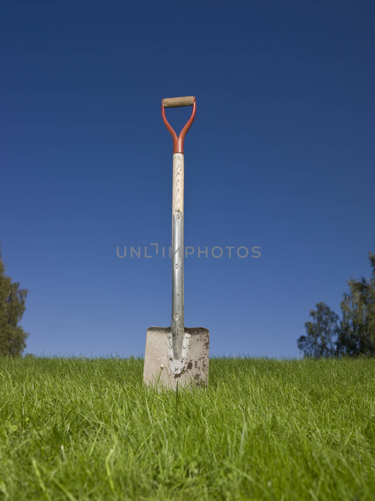 Shovel in green grass against a blue sky