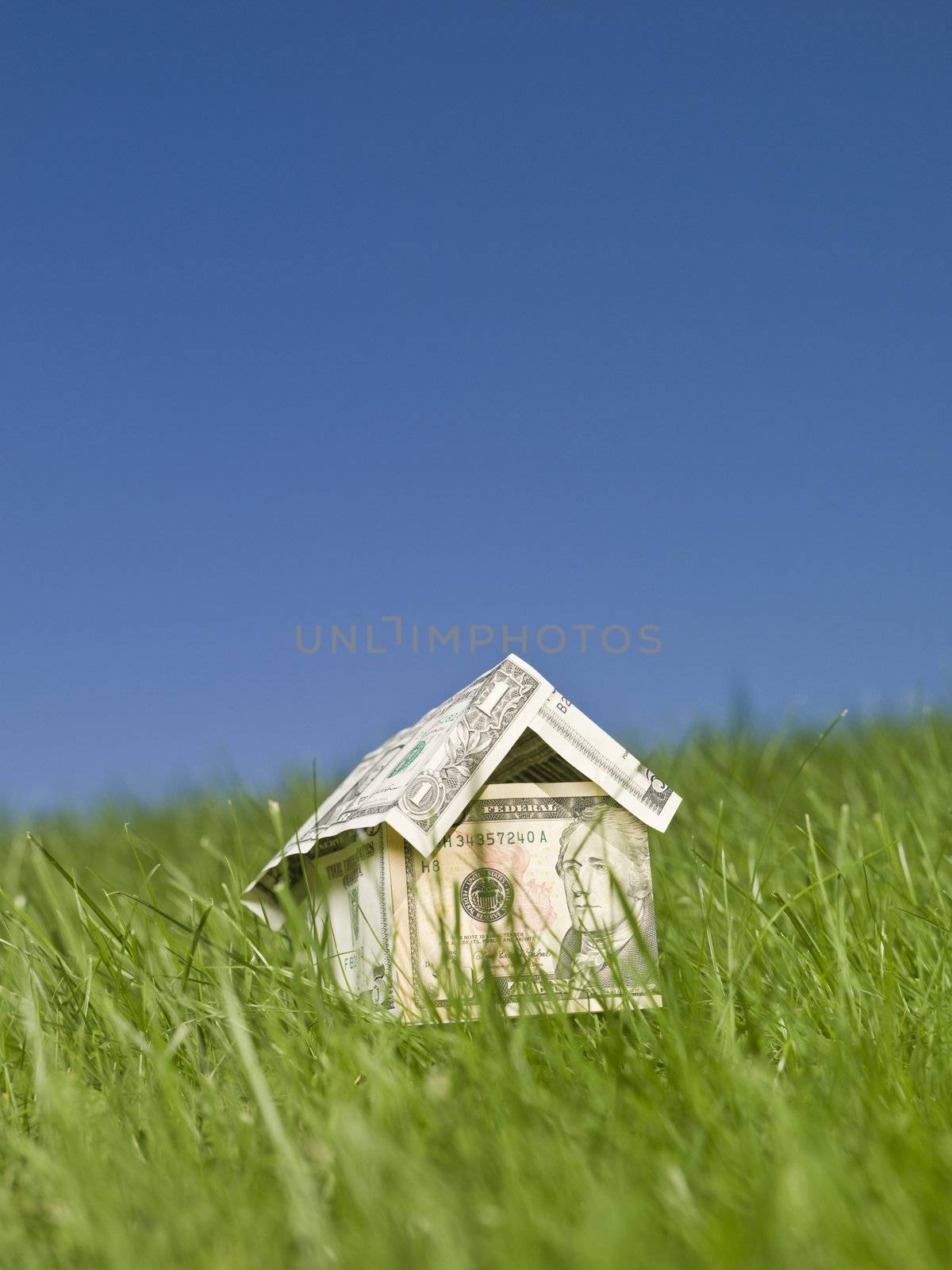 A miniature house made of dollar bills outside in the grass.