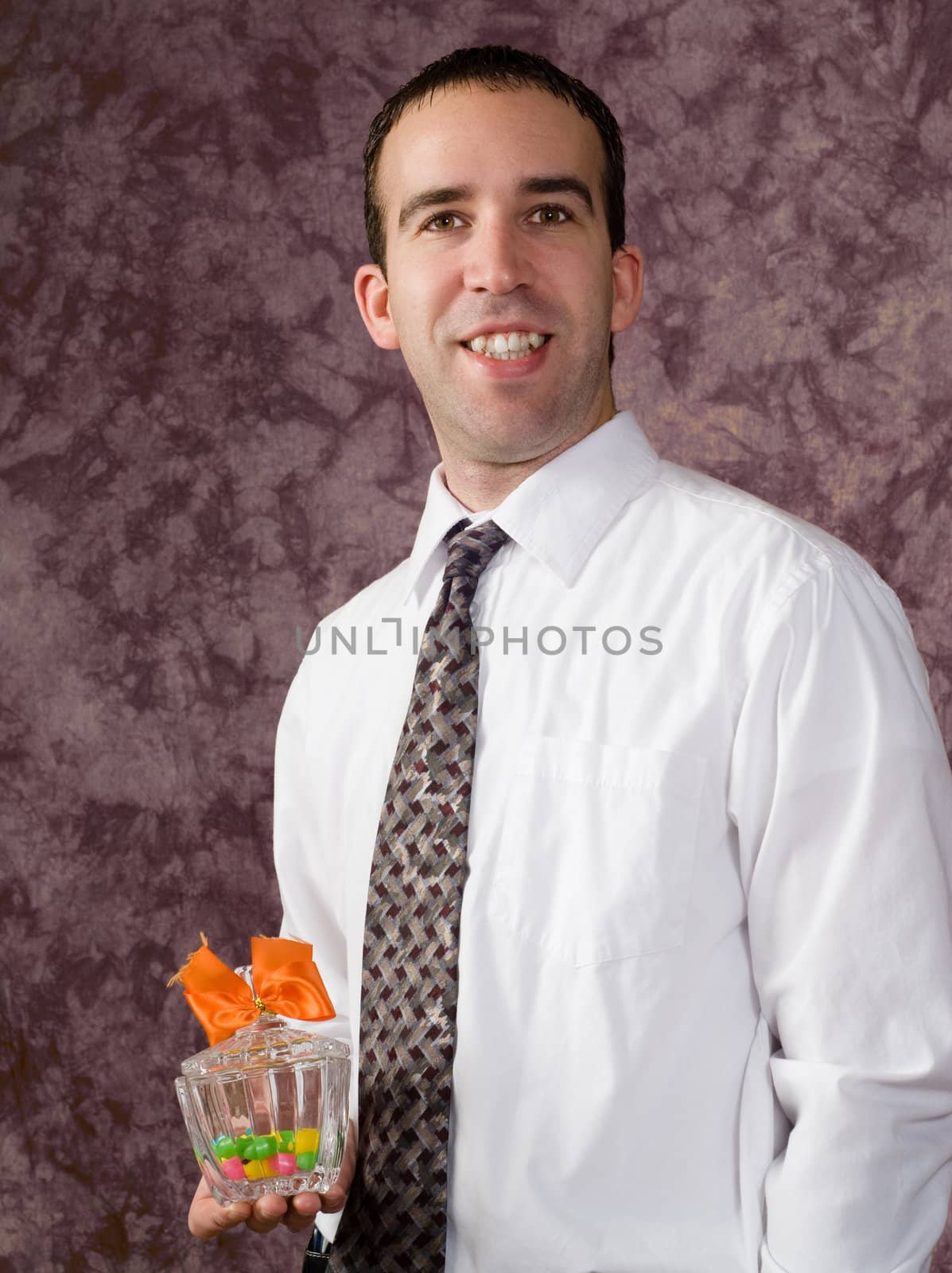 A young man wearing a shirt and tie, holding a candy dish with a bow on it