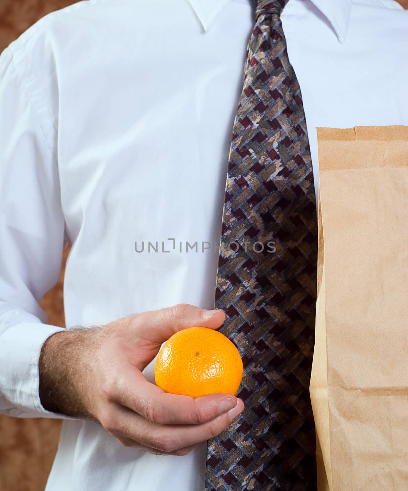 Closeup of a businessman holding his paper bagged lunch and an orange