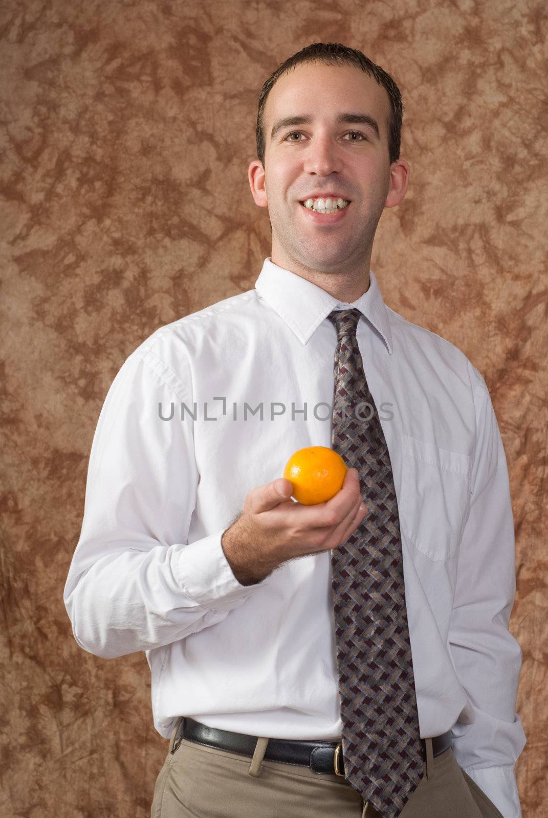 A smiling employee wearing a shirt and tie is holding an orange 