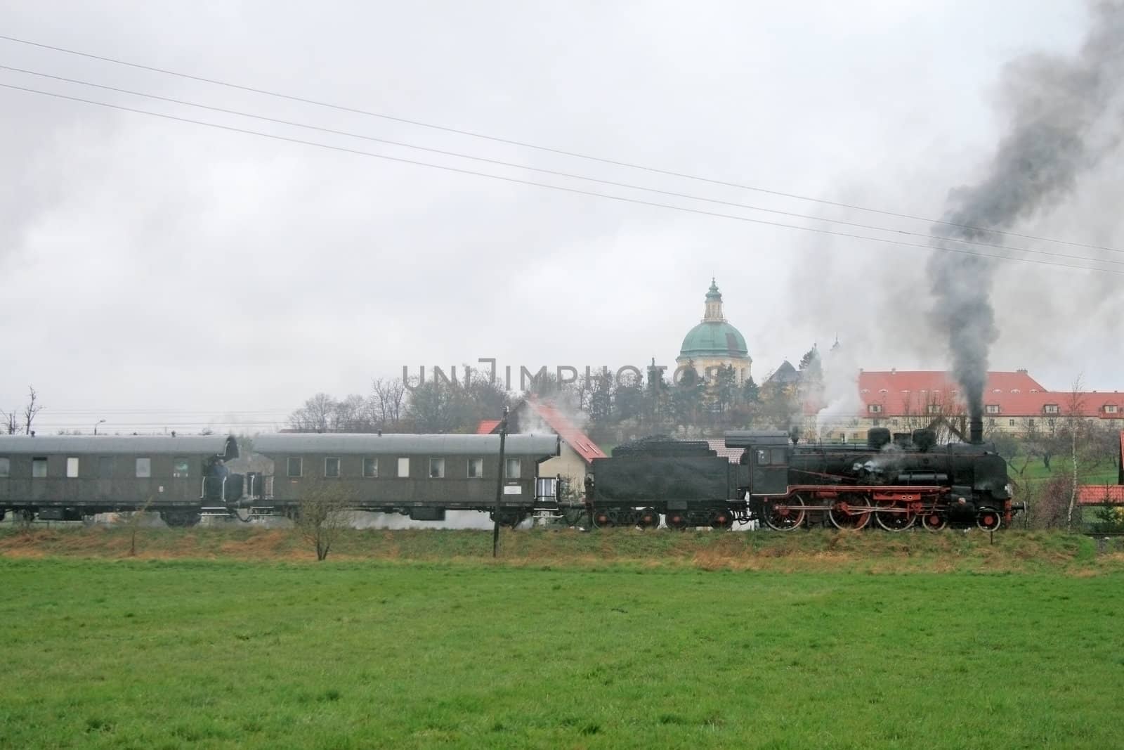 Old retro steam train passing the fields with a palace in background
