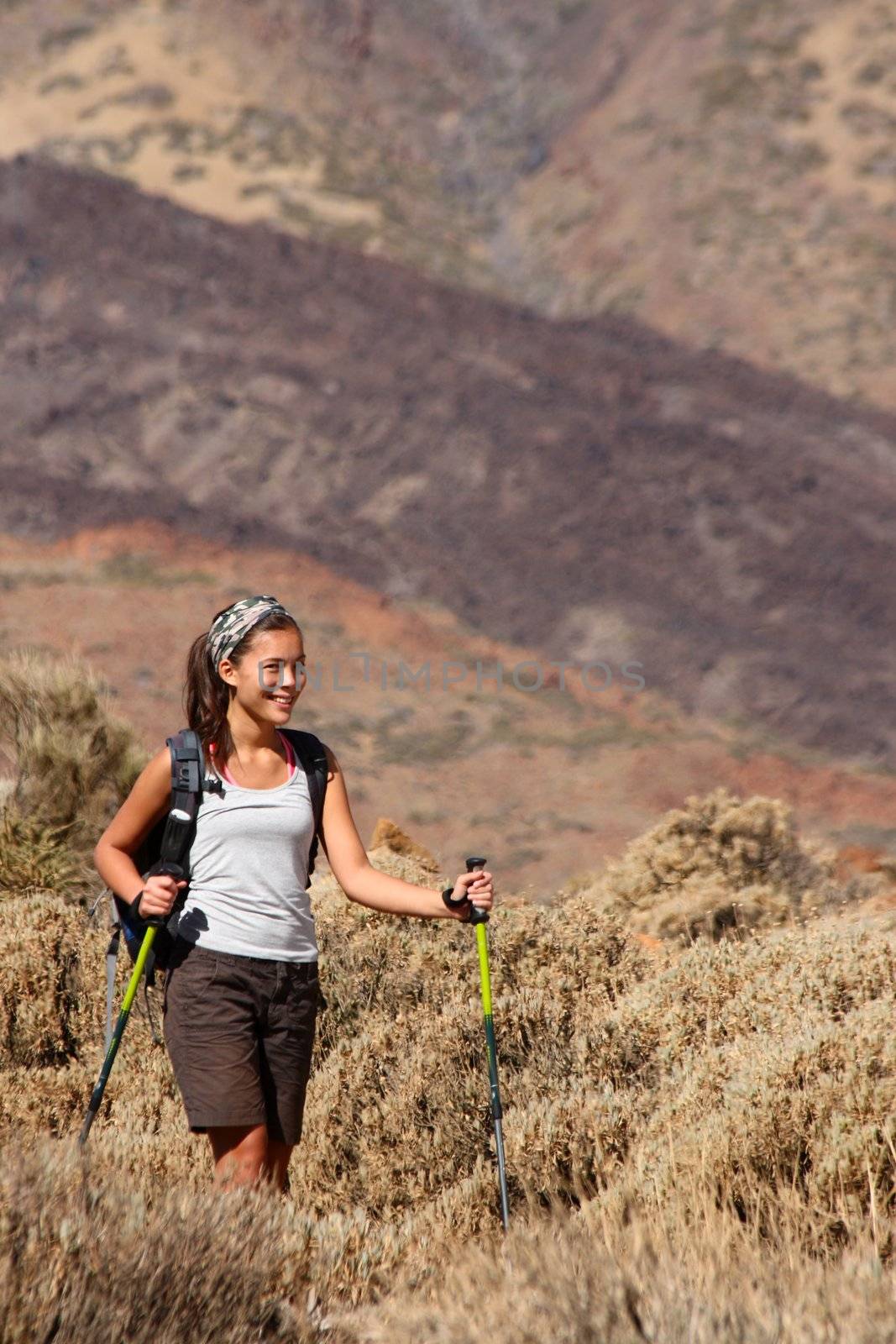 Woman hiking. Young Beautiful mixed race chinese / caucasian female model walking with hiking poles / walking sticks during a hike / backpacking trip in the beautiful and wild volcanic landscape in the national park on the volcano, Teide, Tenerife, Spain. Lot's of copy space!