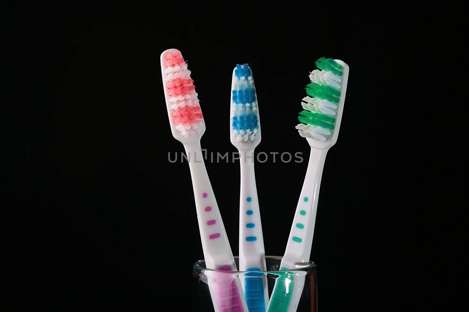 Three tooth-brushes with green and red bristle on black background.