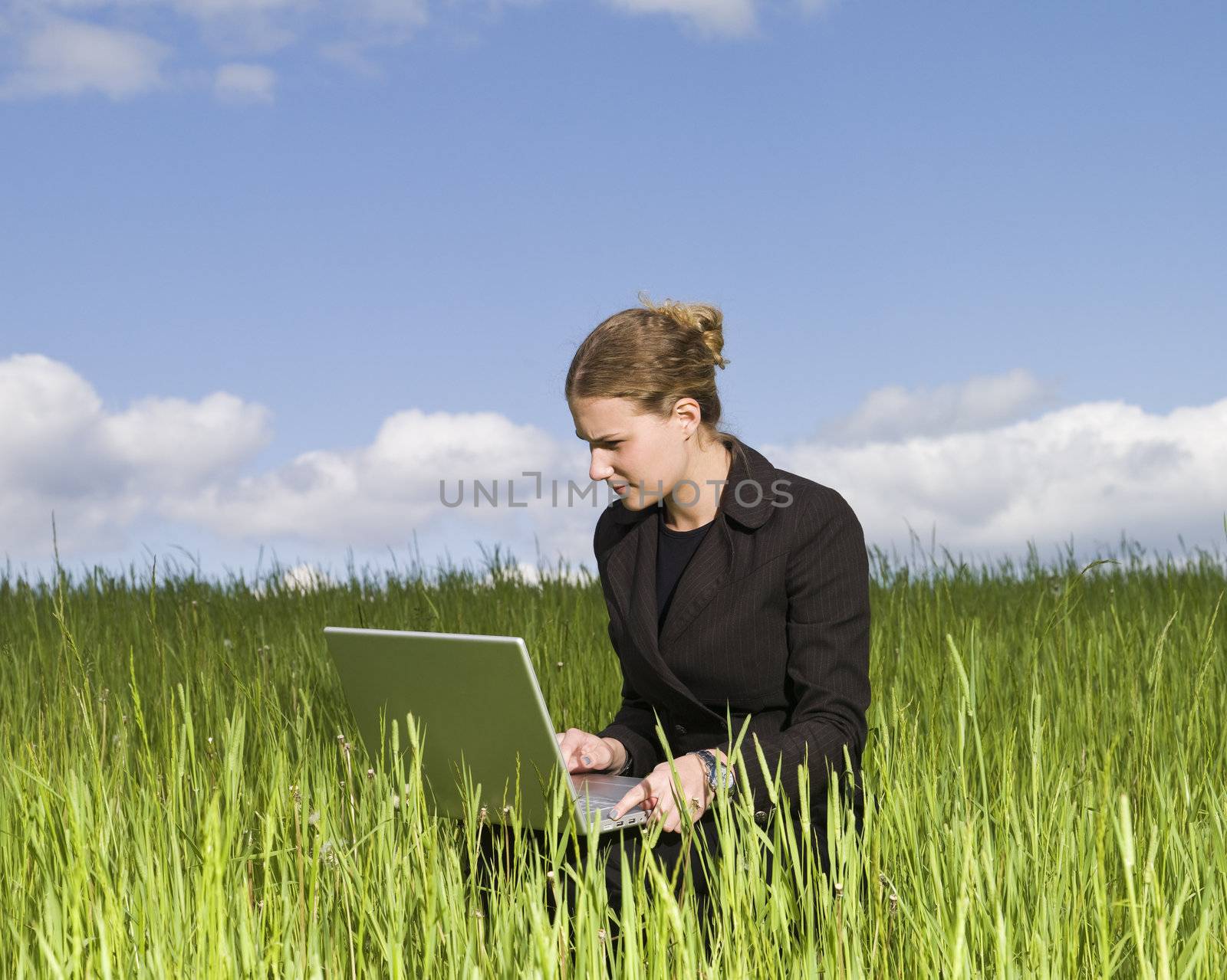 Woman sitting outdoor in thye grass with her laptop by gemenacom