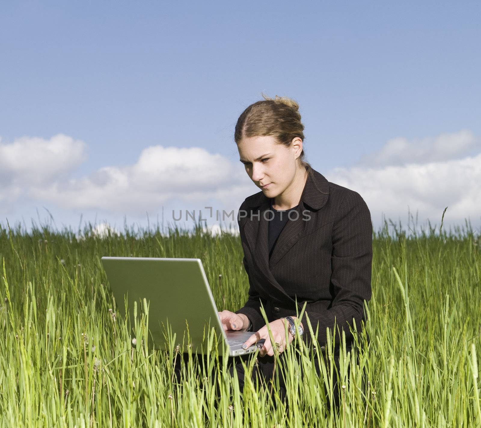 Woman sitting outdoor in the grass with her laptop by gemenacom
