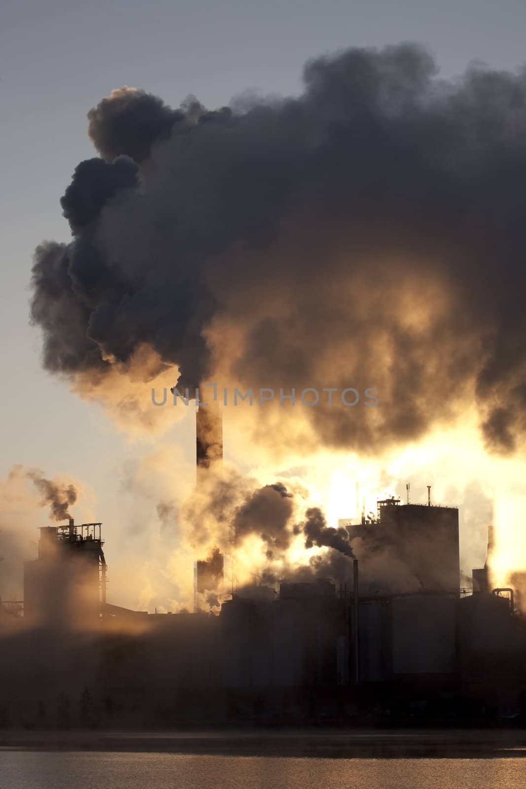 Paper mill covered by heavy smoke screen by hazy sunrise.