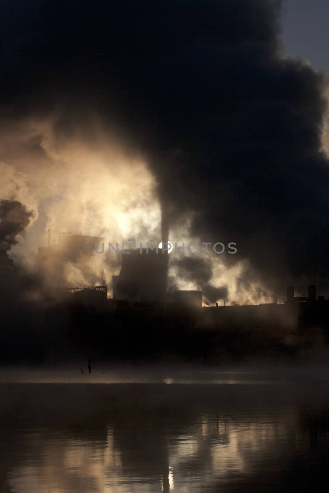 Paper mill covered by heavy smoke screen by hazy sunrise.