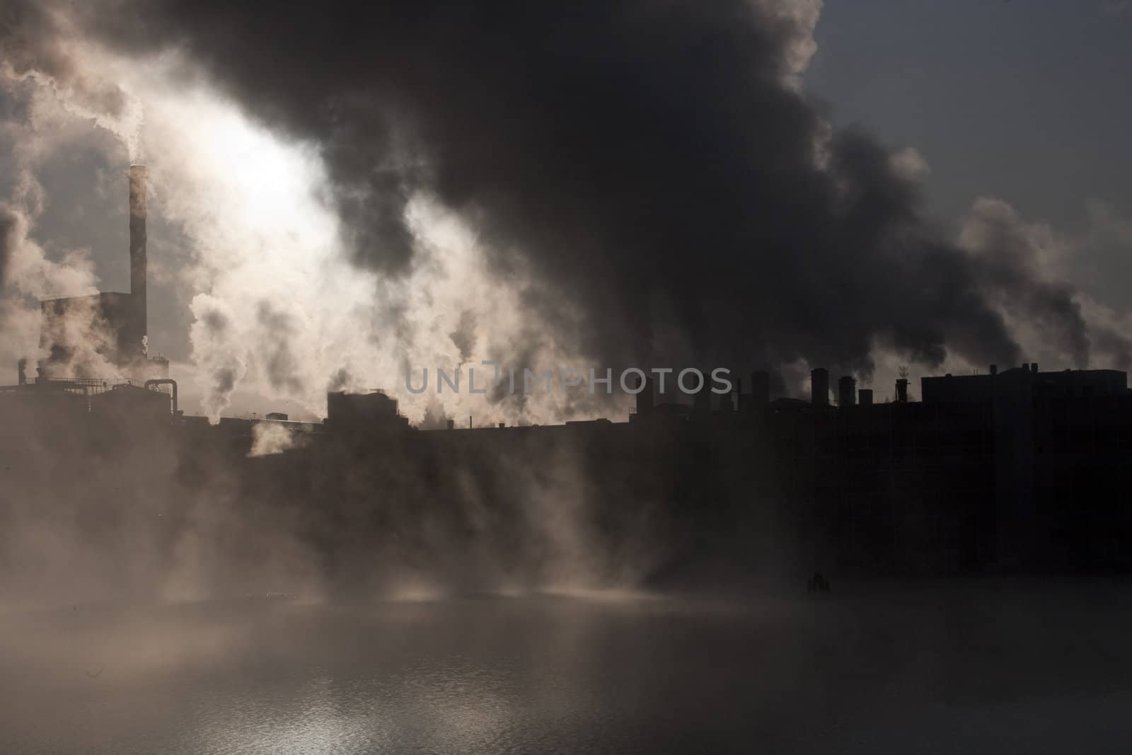 Paper mill covered by heavy smoke screen by hazy sunrise.