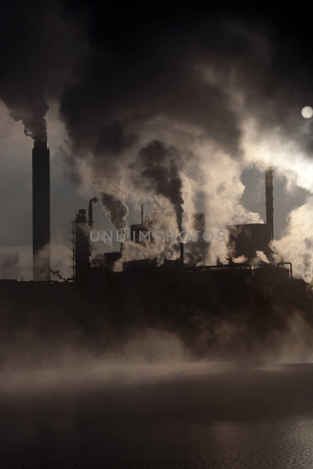 Paper mill covered by heavy smoke screen by hazy sunrise.