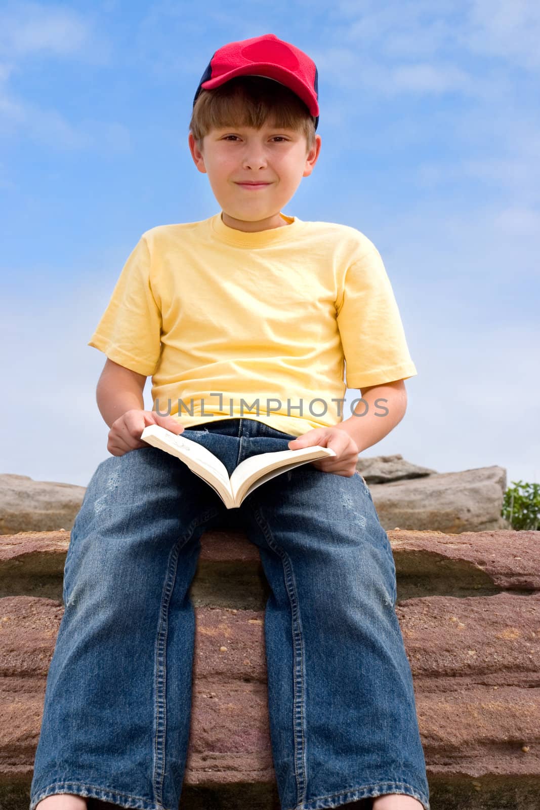 Child holding a book sitting against blue sky