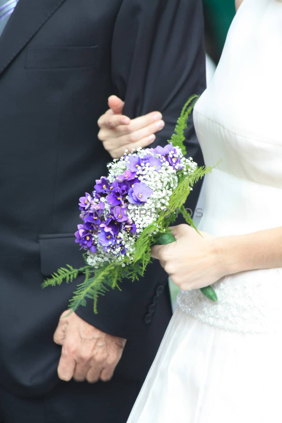 A bride walking to the church, holding her purple wedding bouquet