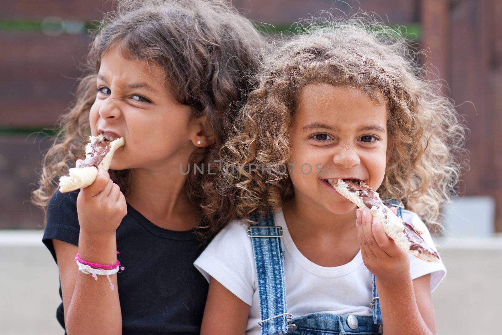 Sisters crunching heartily into a slice of bread with chocolate