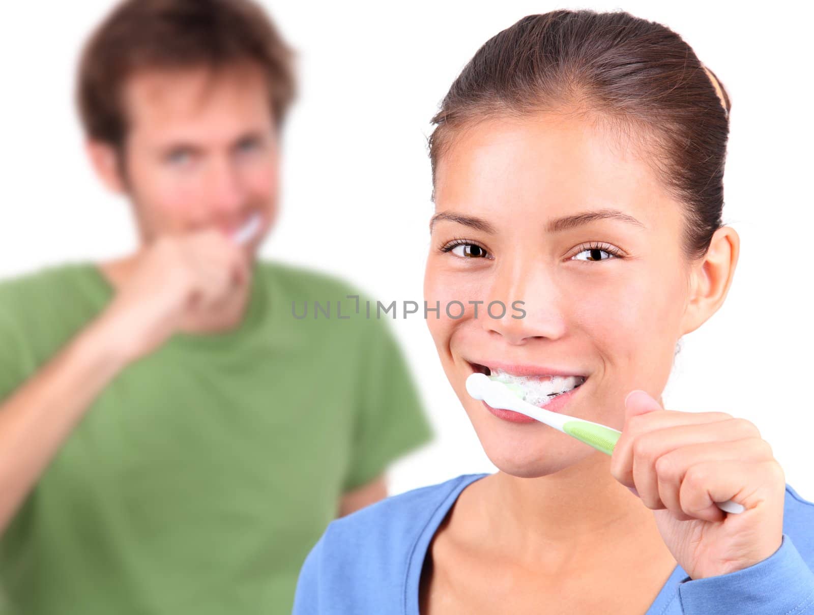 Young mixed race couple brushing teeth together on white background.