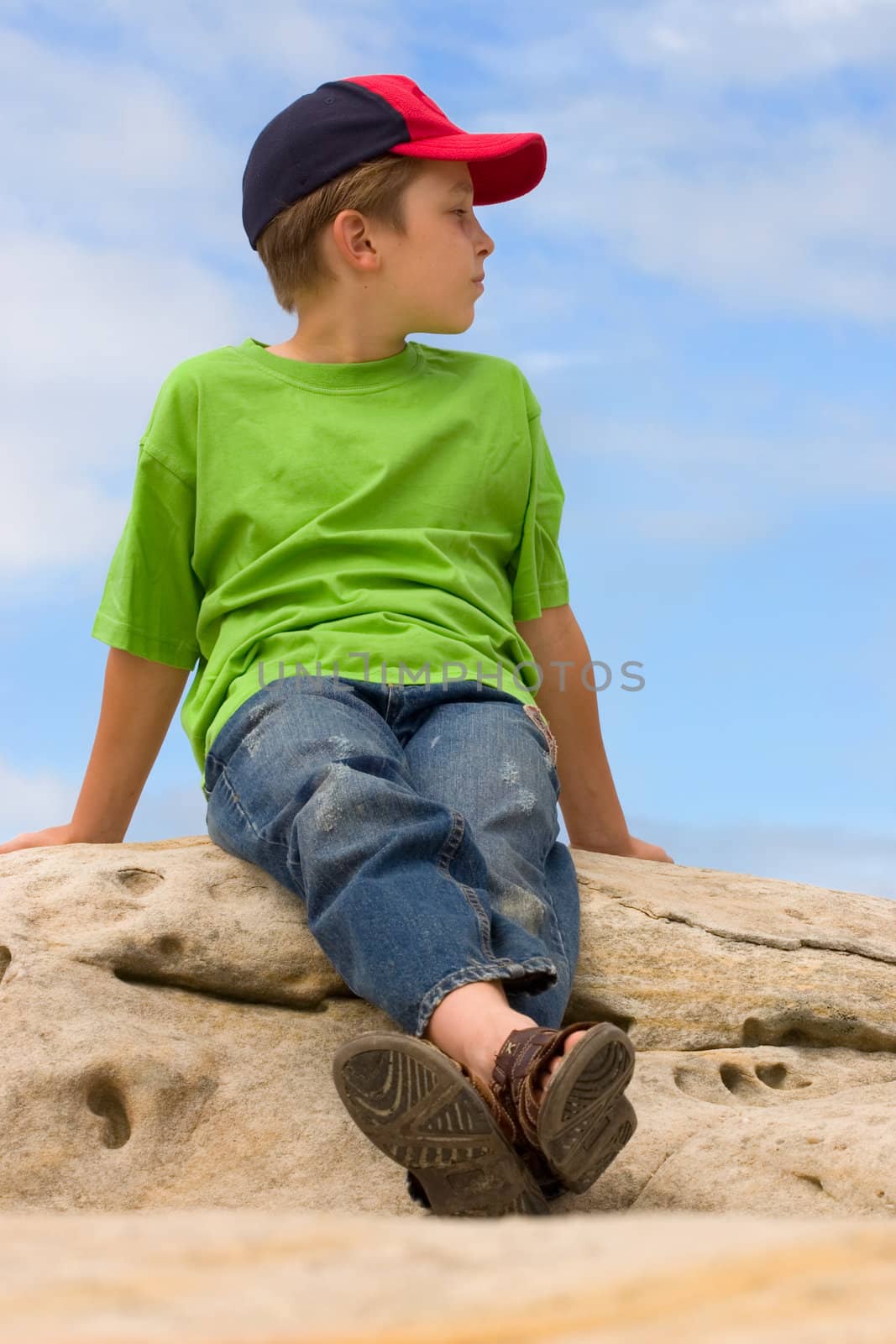 Laid Back Child sitting on a rock against a beautiful blue sky by lovleah