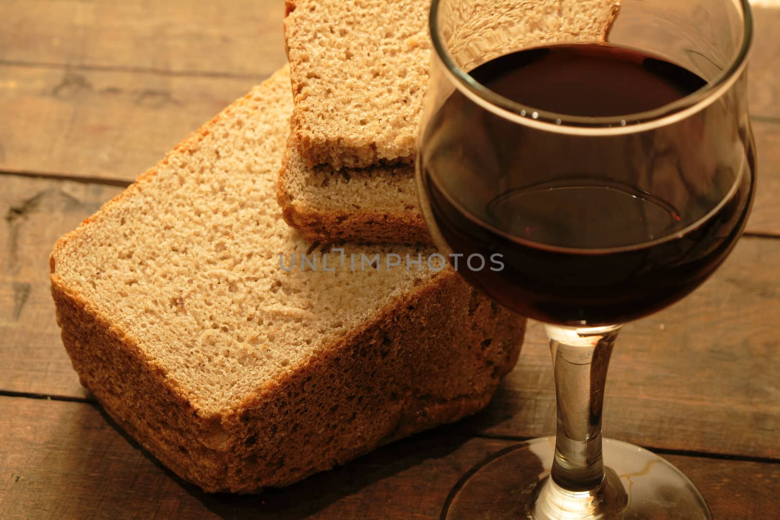 Closeup of rye bread and goblet of red wine on wooden background