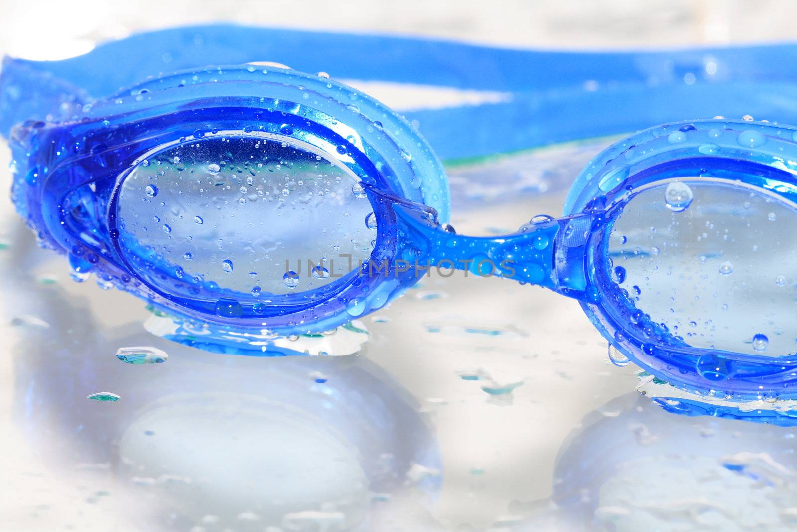 Closeup of blue wet swimming goggles on glass background with water drops