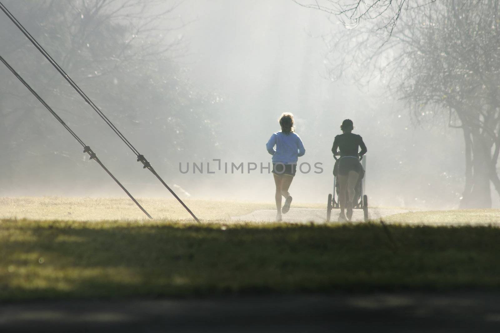 Two joggers one with a baby stroller exercise despite the misty fog.