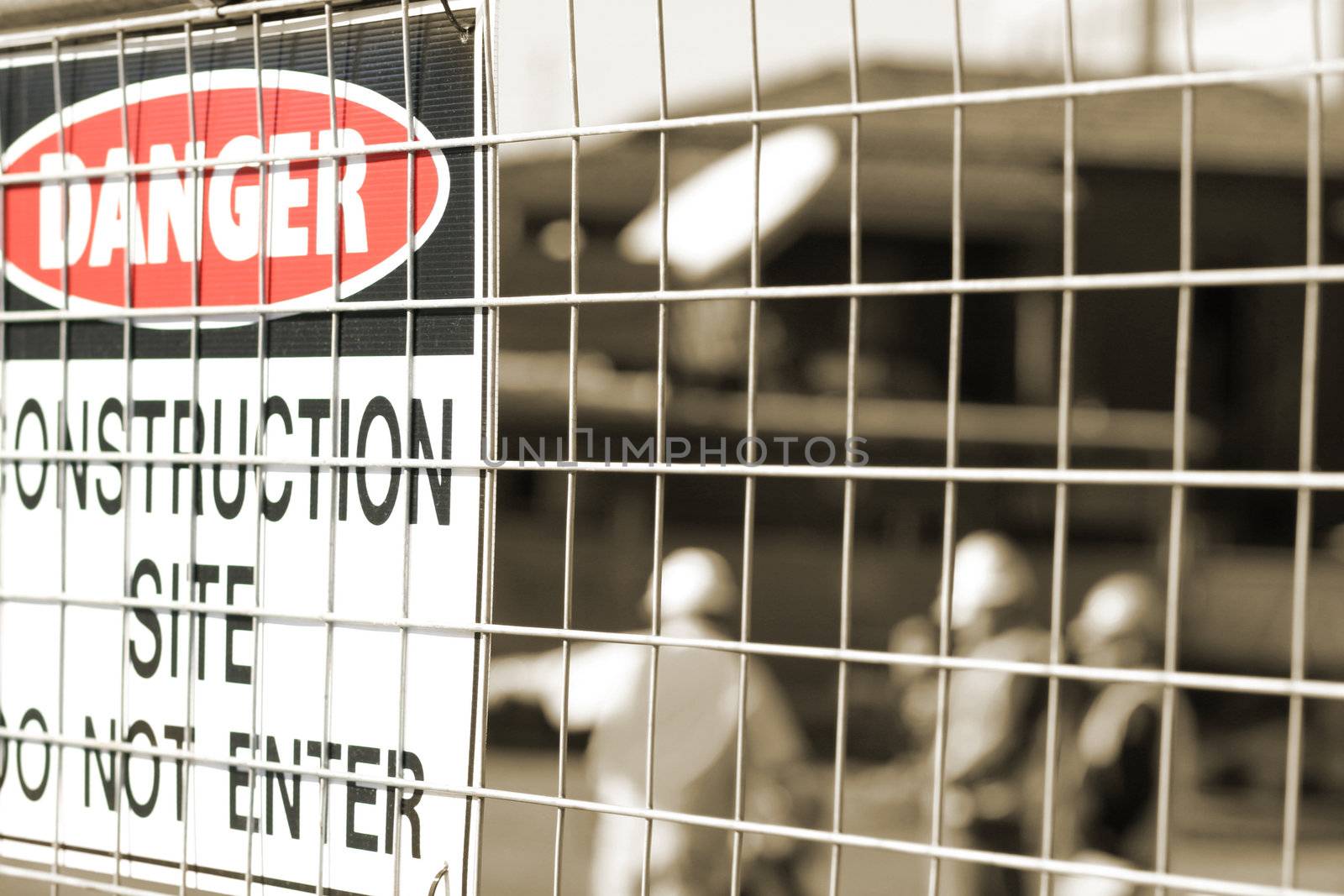 Sign and construction workers out of focus behind the fence. 