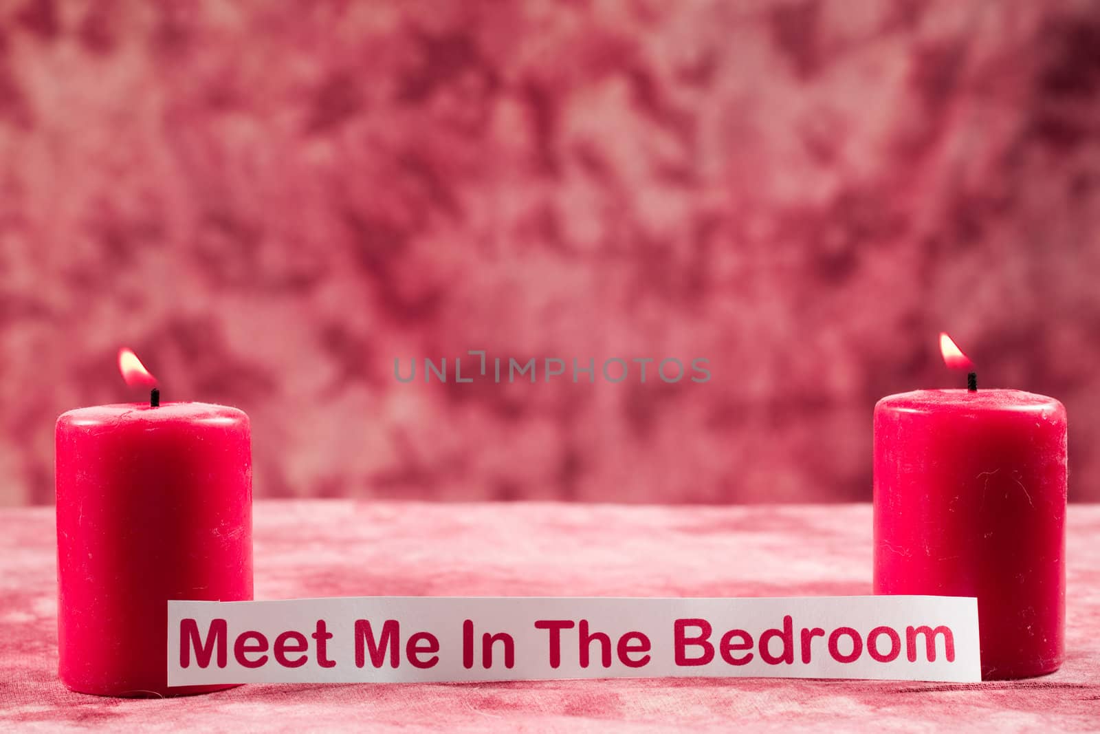 Two burning candles shot with a note in front of them which says meet me in the bedroom