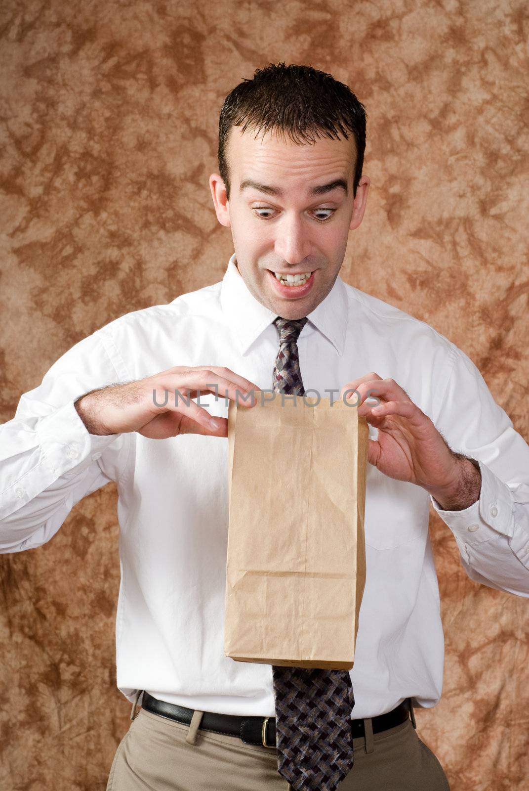 An employee wearing a tie is looking happy about what he sees in his paper lunch bag
