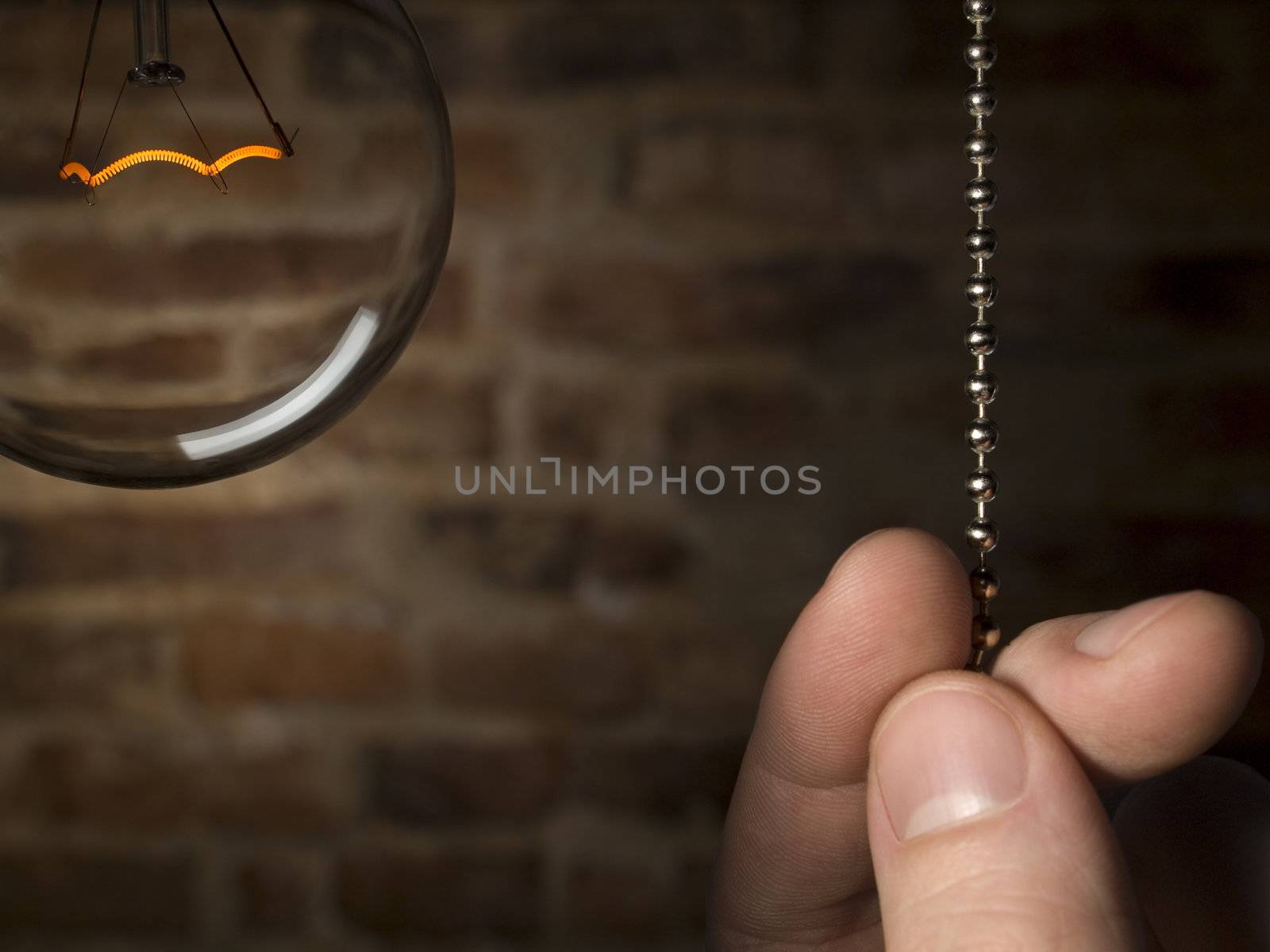 A man's hand is about to switch off the bulb light. Brick wall as background.