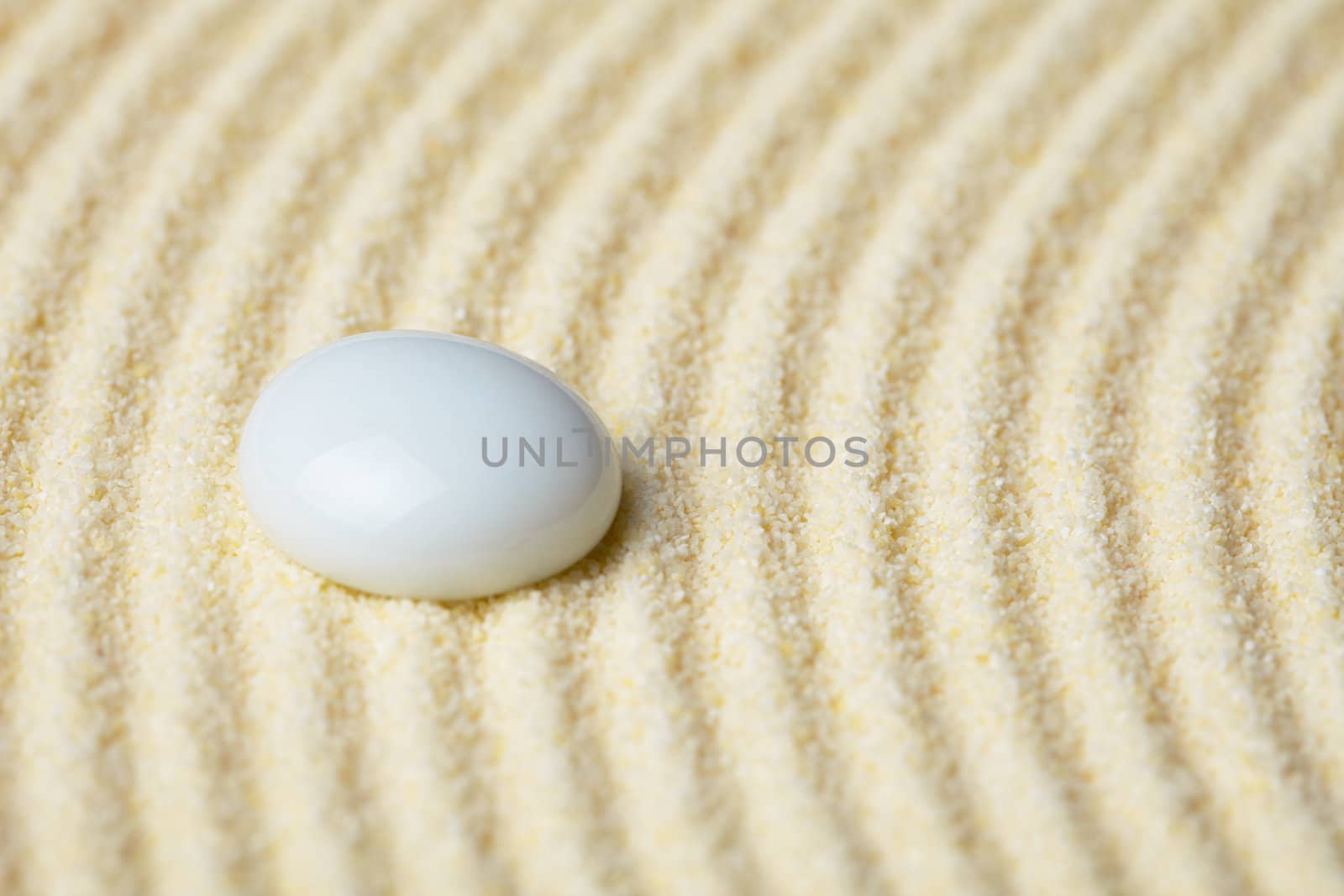 Round ceramic stone on a surface of yellow sand close up
