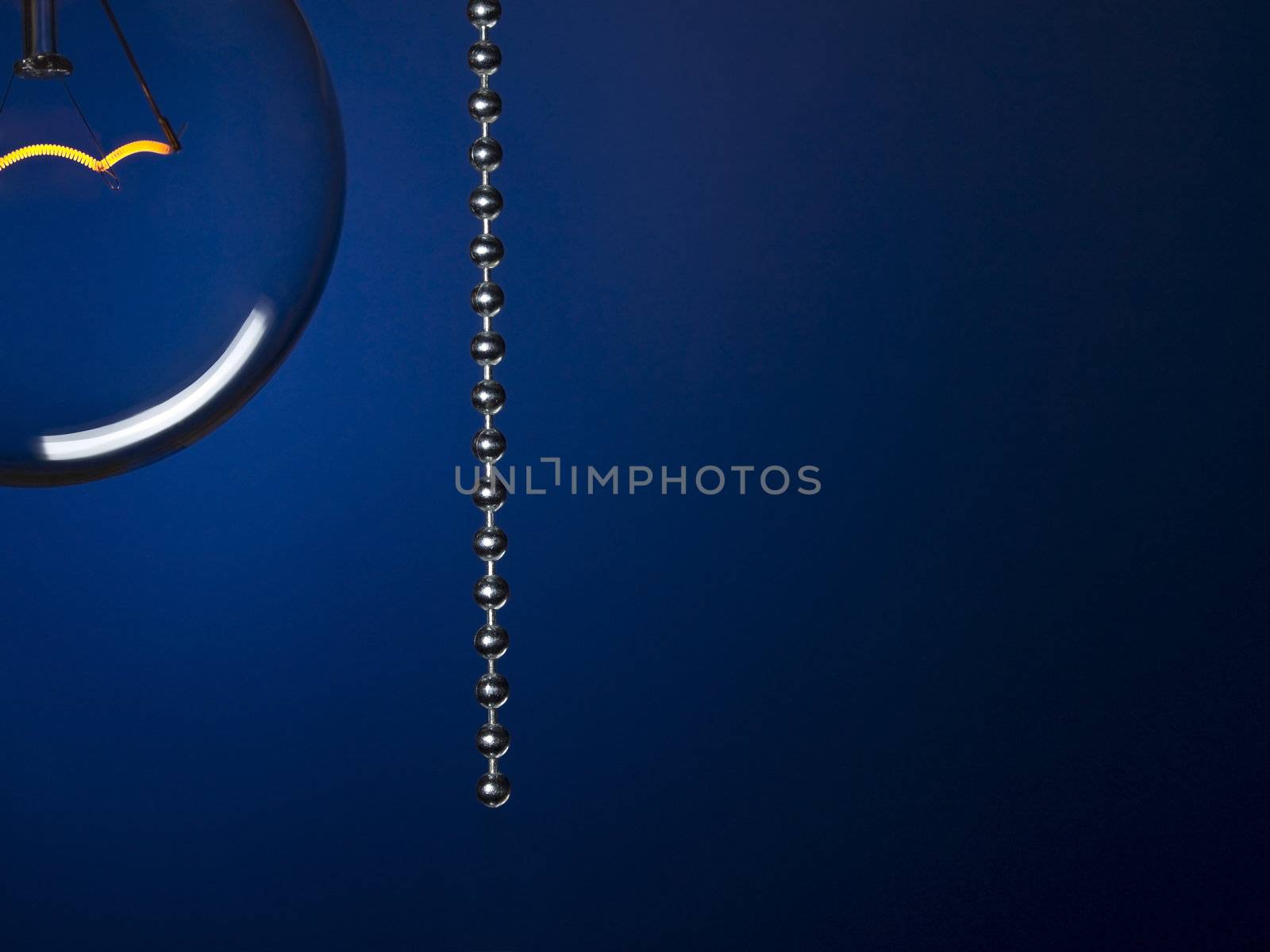 Close up on a transparent light bulb with a pull switch over a blue background.