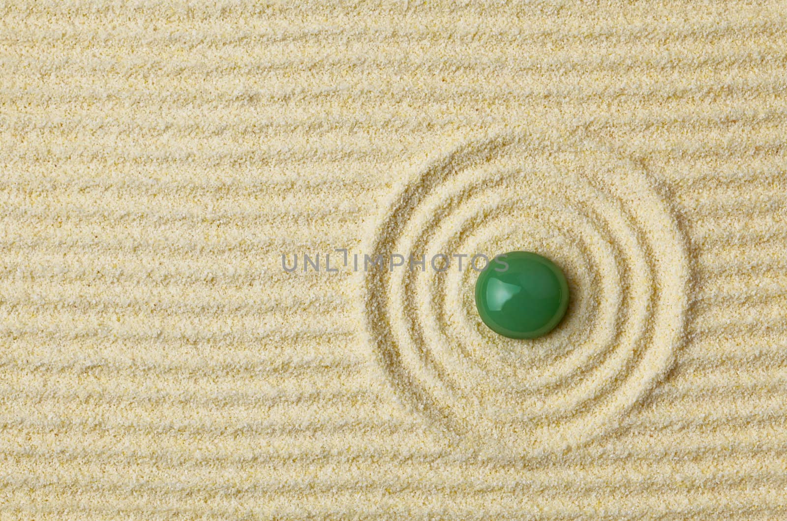 Round green stone on a surface of yellow sand