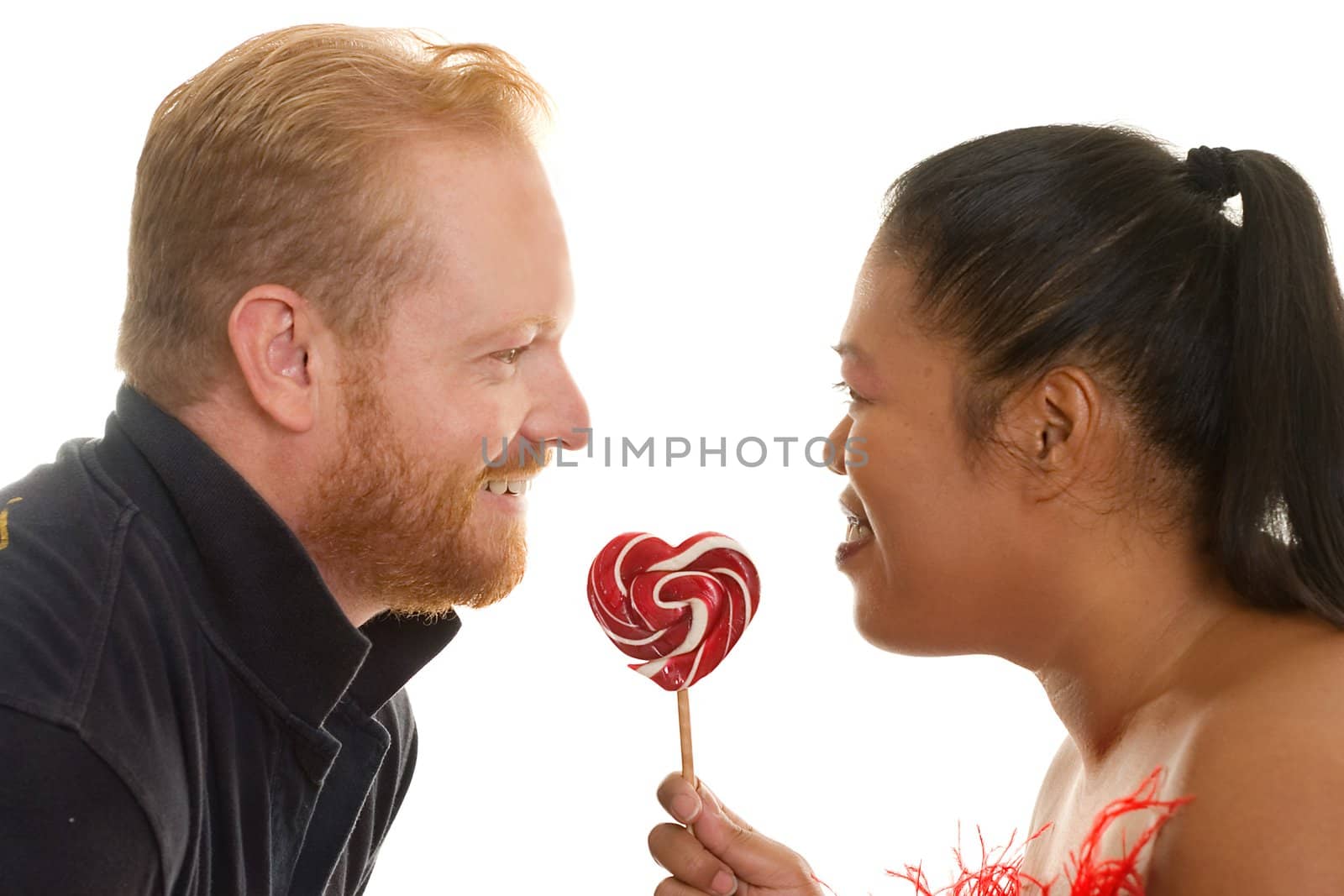 Diversity couple facing each other with a red and white candy.  Focus to lollipop