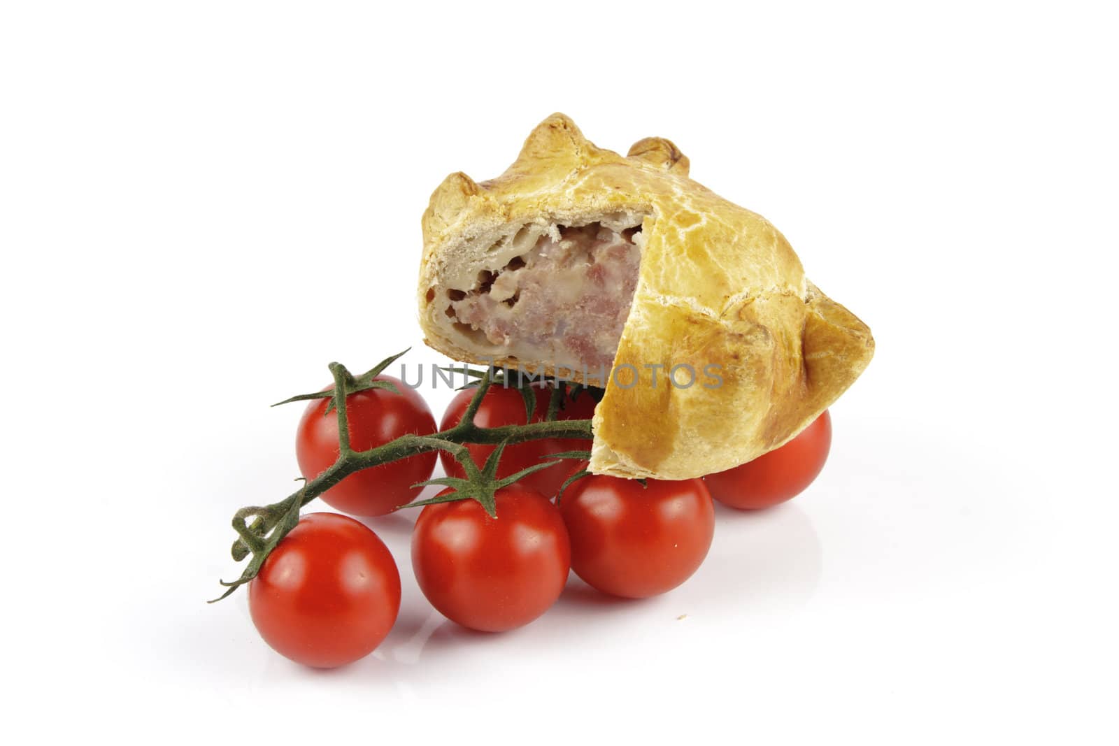 Contradiction between healthy food and junk food using tomatoes and a pork pie on a reflective white background 