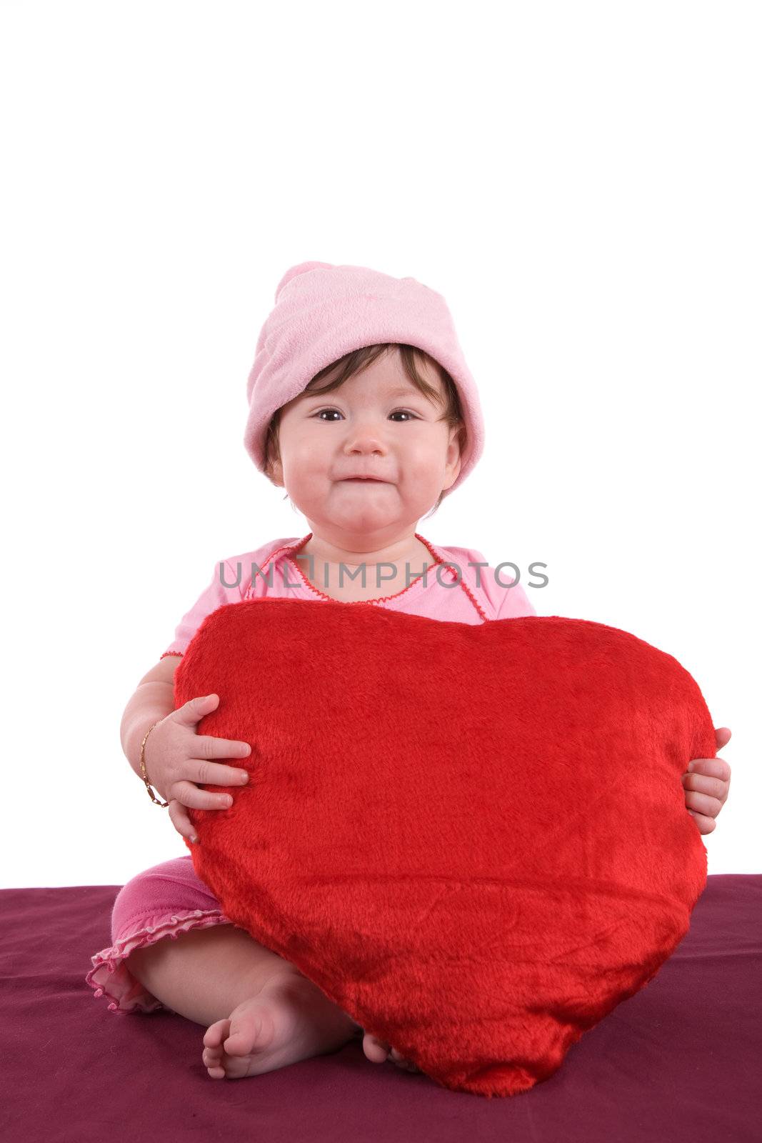 Cute baby holding a big red heart and wearing a small pink hat