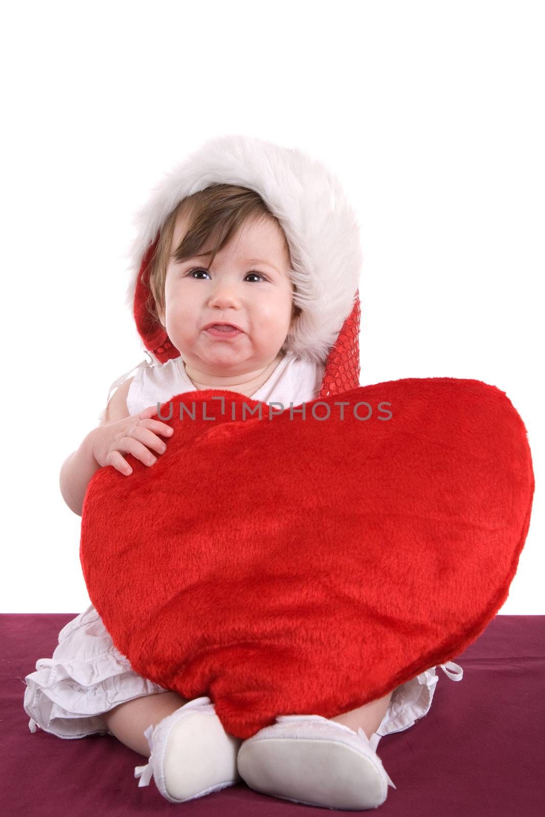 Cute baby girl holding a big red heart and wearing a santa hat