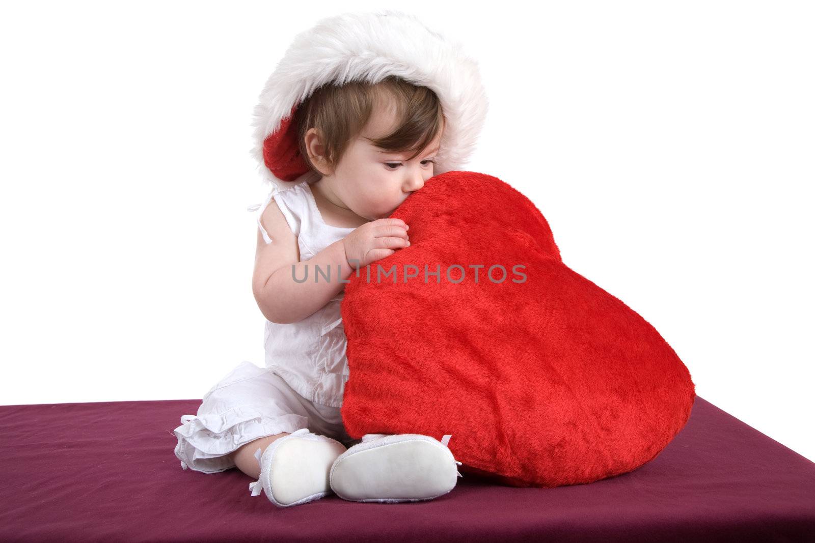 Cute little kid hugging a big soft red heart with a christmas hat