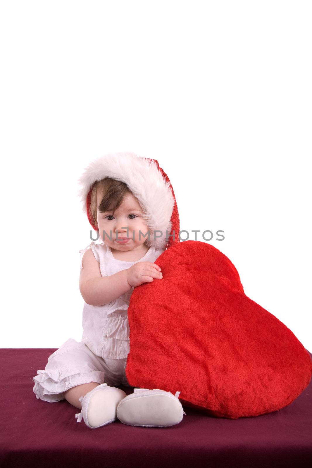 Cute little baby holding a big red heart and wearing a santa hat