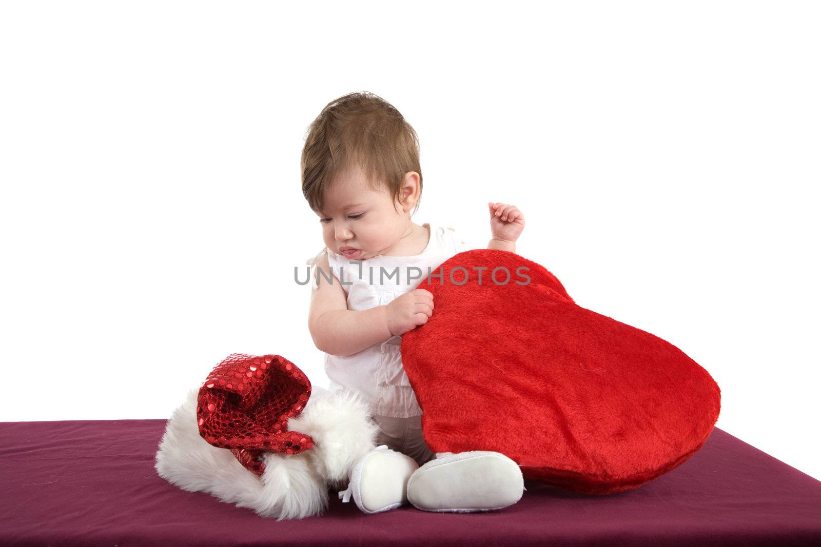 Cute little baby girl looking a bit surprised at the santa hat next to her