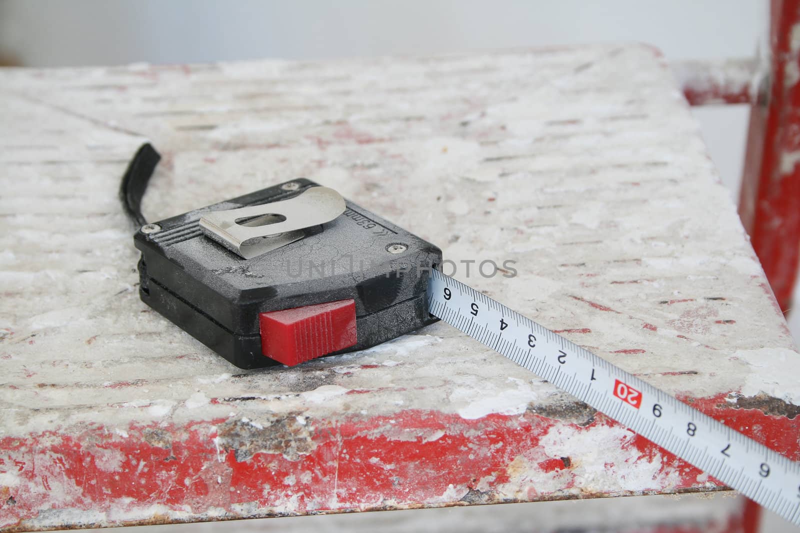 The black tape measure lays on a step-ladder