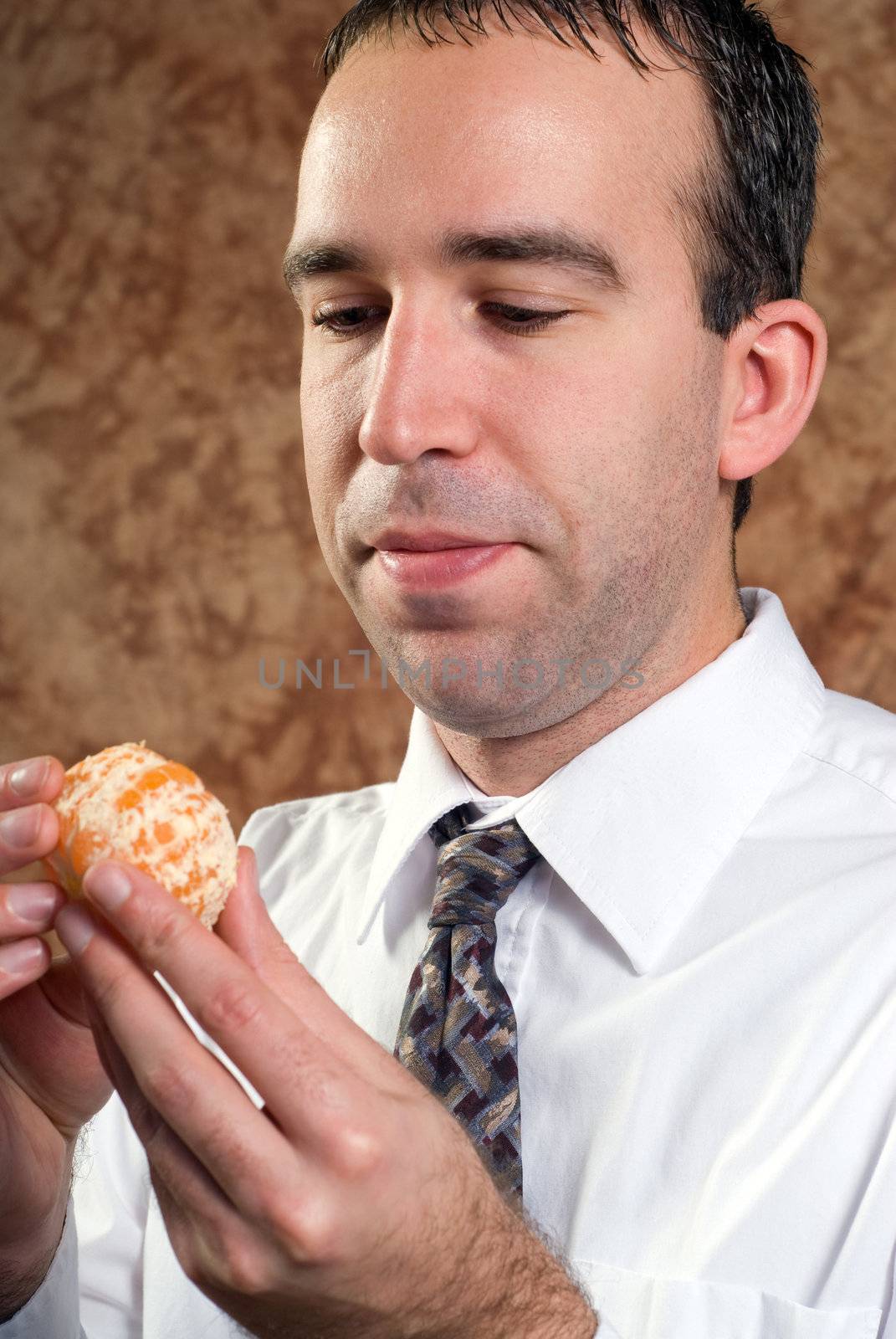 A young businessman wearing a white shirt and tie is holding a peeled orange