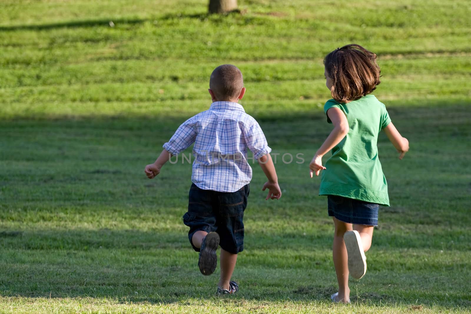 A little boy and girl run through the grassy field without a care in the world.