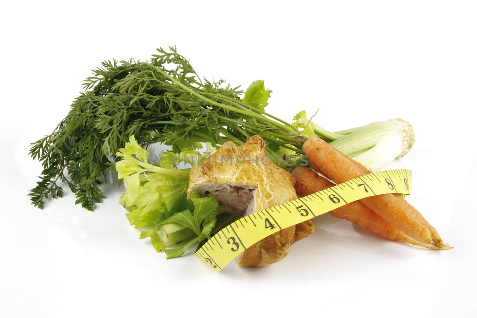 Contradiction between healthy food and junk food using a bunch of carrots and pork pie with a tape measure on a reflective white background 