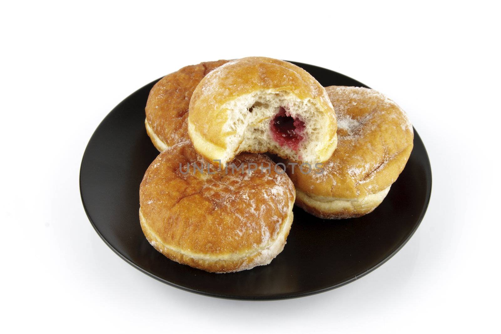 Black round plate of jam doughnuts with a bite mark on one showing red jam on a reflective white background