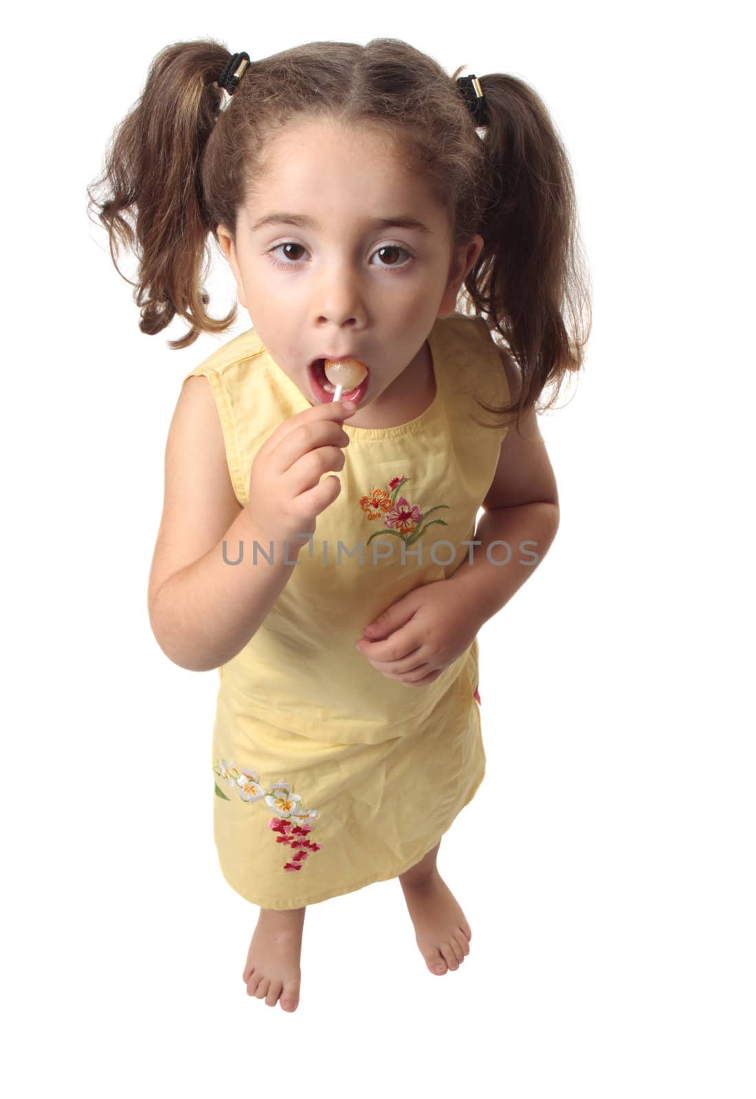 A little girl sucking on a lollipop candy.  She is dressed in a yellow outfit and has her hair in ponytails.