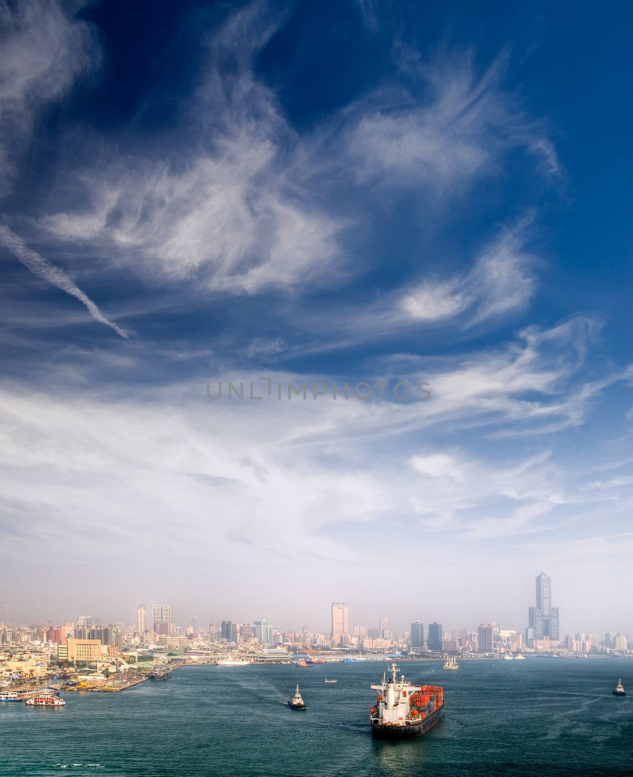 Harbor with boats and skyscraper under dramatic sky in Kaohsiung, Taiwan.