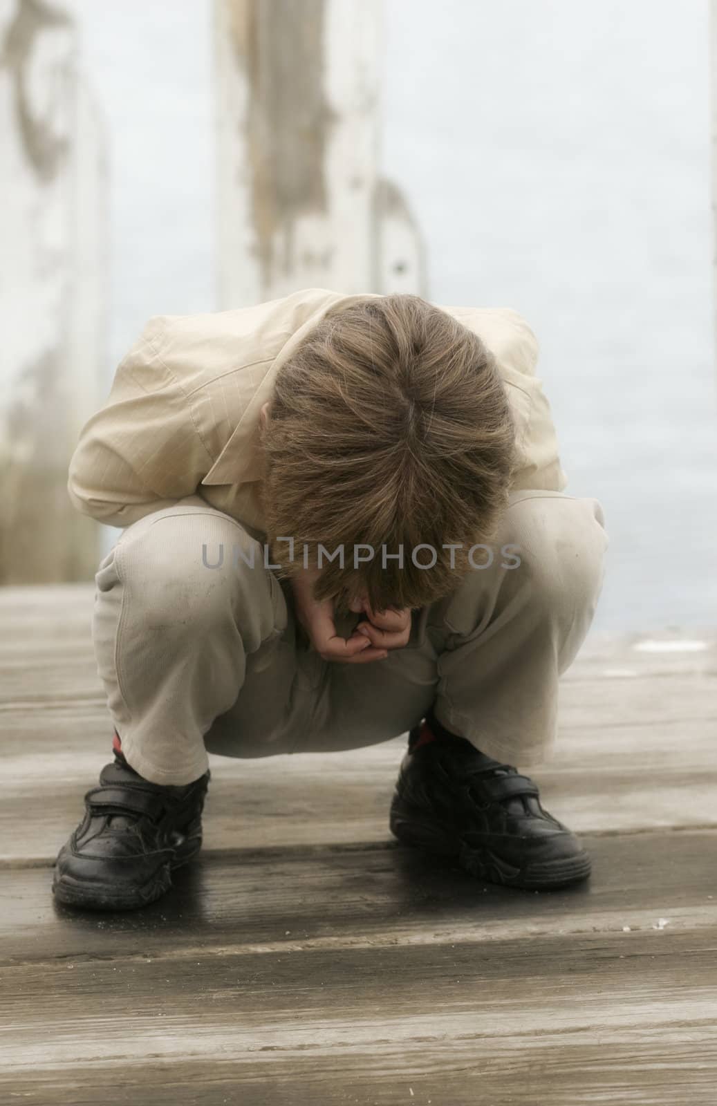 young child looking through the spaces cracks in a wooden deck pier.