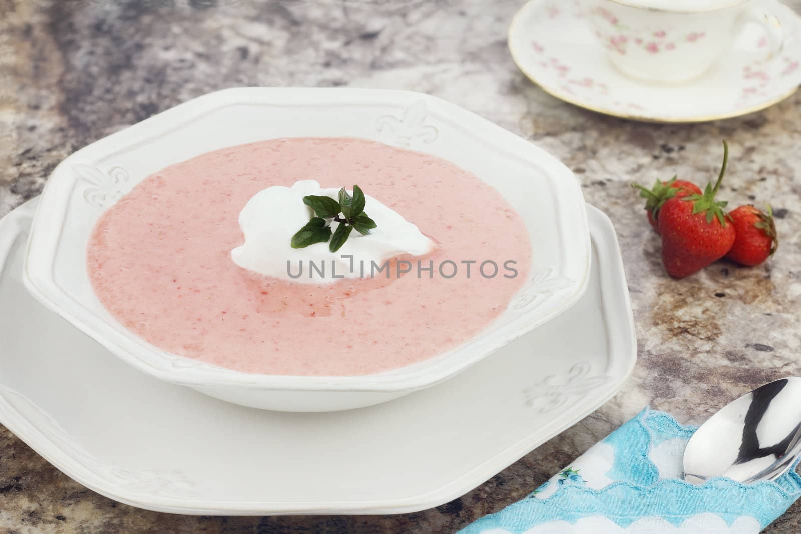 A bowl of chilled strawberry soup, garnished with a dollop of whipped cream and a fresh sprig of chocolate mint.

