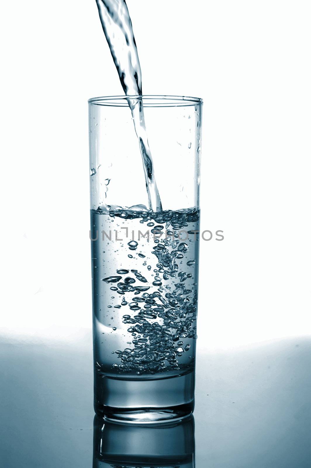 glass with pouring water with reflection on white