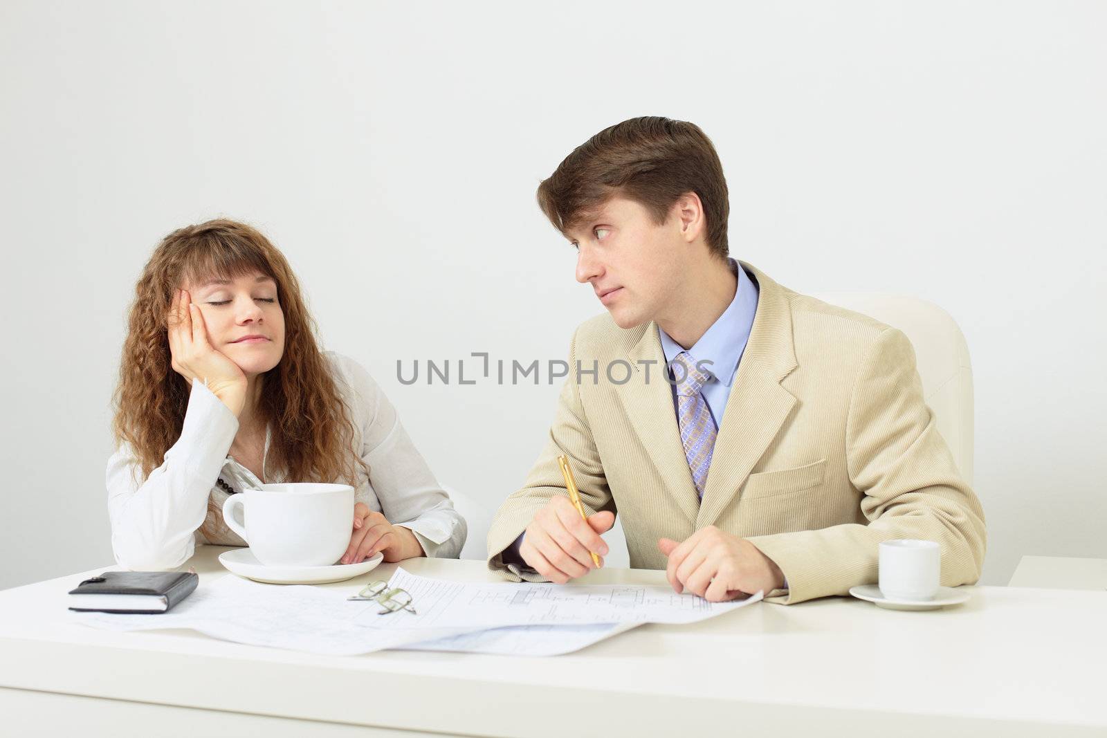 The woman falls asleep sitting at a table with a huge cup of coffee