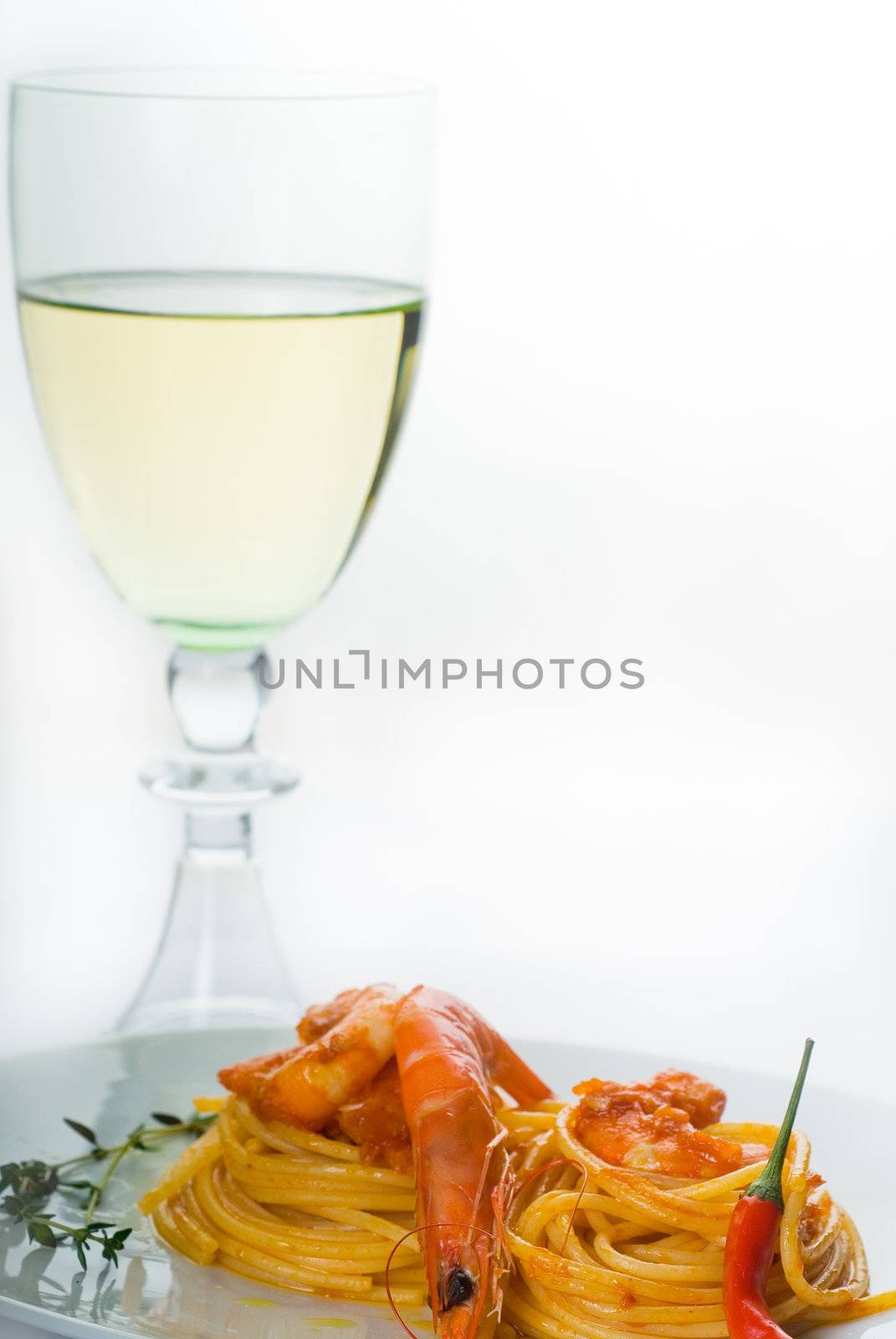 italian spaghetti pasta and fresh spicy shrimps sauce,with a grass of dry white wine on background