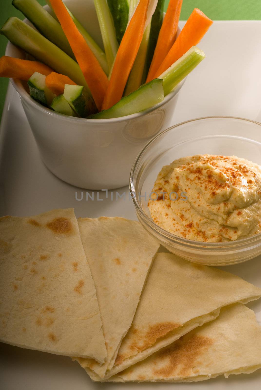 middle eastern hummus dip on a glass bowl with homemade pita bread and raw vegetable